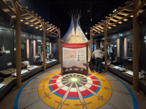 Sovereign Nations exhibit in the Montana Heritage Center’s Homeland Gallery, featuring a tepee backdrop, interpretive panels, and tribal homelands compass on the floor. Photo by Sarah Bolt, Tempest Technologies.