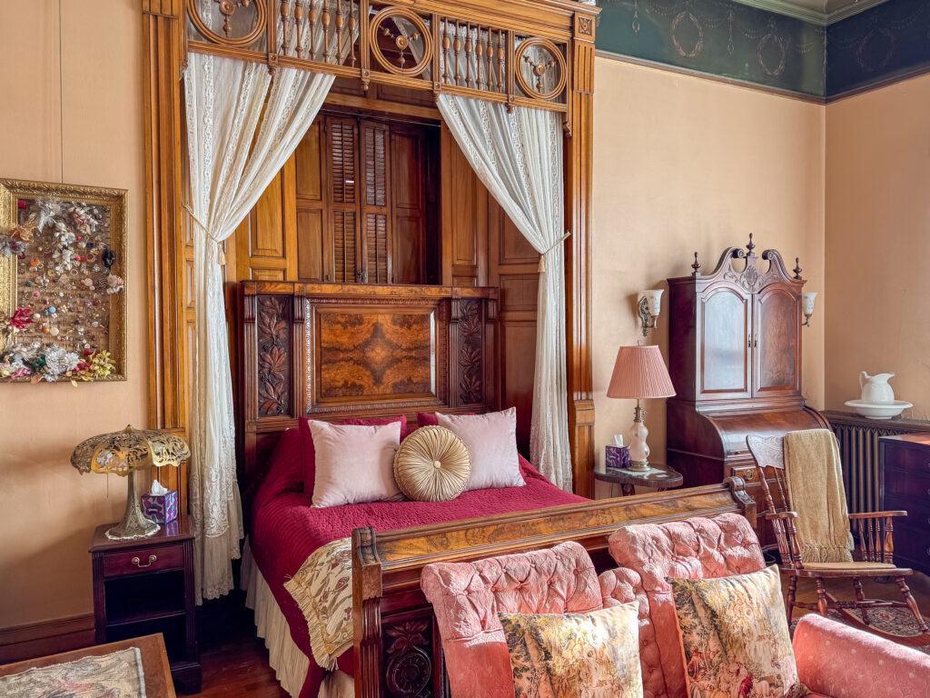 Master suite at Copper King Mansion bed and breakfast in Butte, Montana with ornate wood canopy bed, vintage furniture, and lace curtains. Photo by Sarah Bolt, Tempest Technologies.