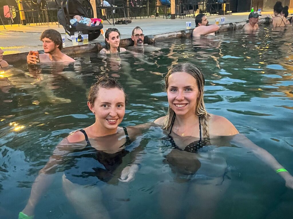 Two people smiling while soaking at Norris Hot Springs near Bozeman, Montana. Geothermal mineral pool and popular Southwest Montana hot springs stop for relaxation and wellness. Photo by @kati_explores on Instagram.
